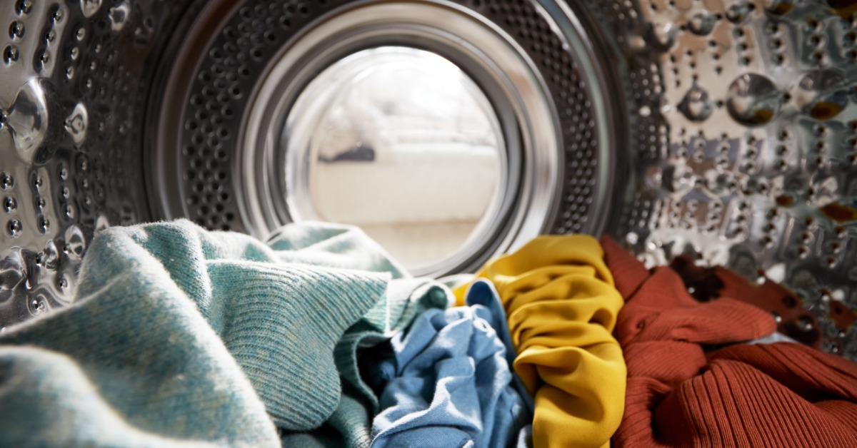 Colorful clothes lying inside a metal washing machine drum with water drops on the textured inner wall.