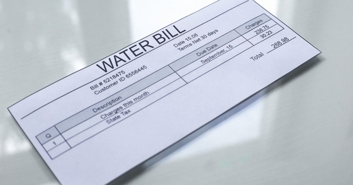 A paper water bill lying on a pale table with printed charges, dates, and a total amount displayed clearly.