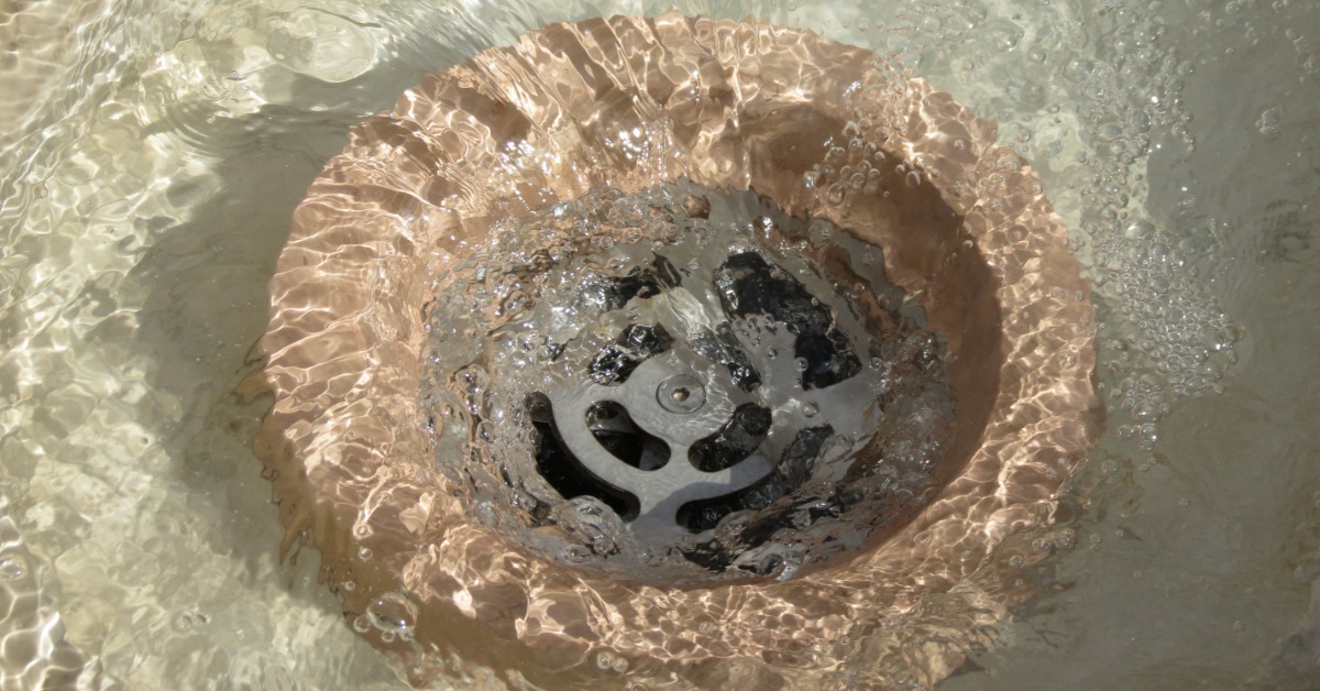 A round metal drain surrounded by rippling water, bubbles, and light reflections in a shallow basin.